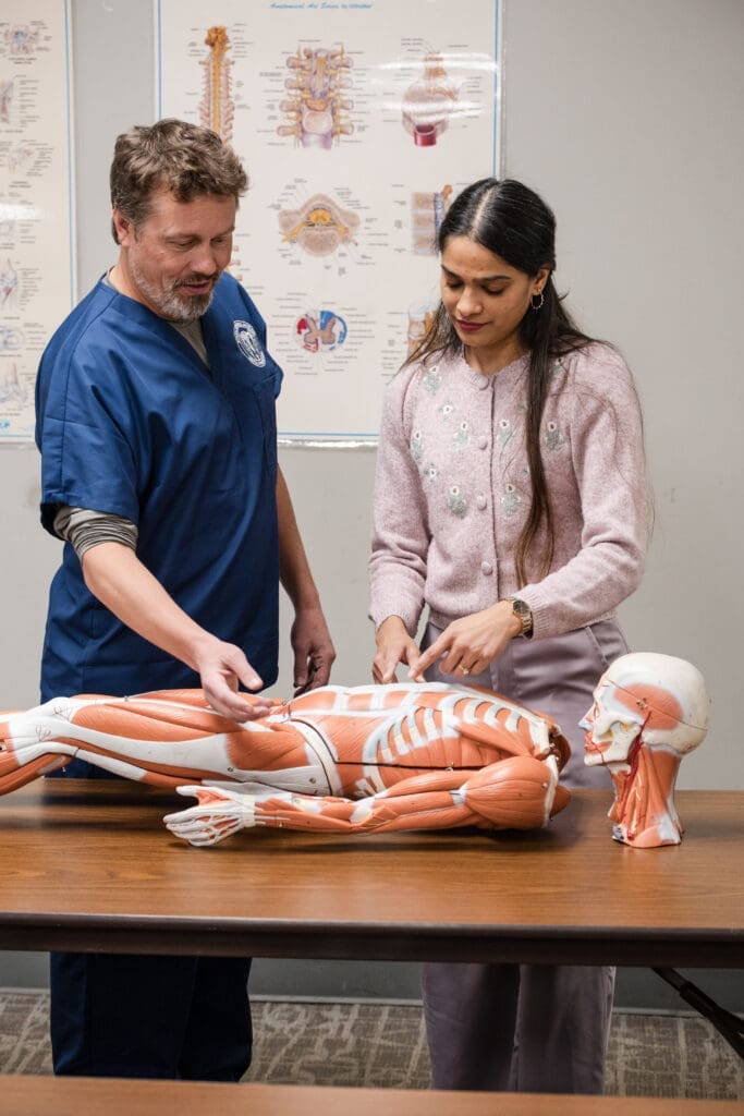 A medical massage student and instructor looking at an anatomical dummy